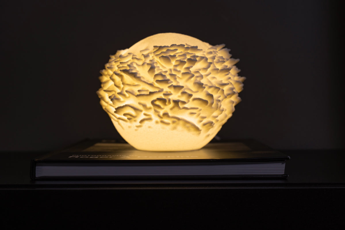 Atoll mini sfeerlamp brandend tegen een donkere achtergrond met sterk licht- en schaduwspel.