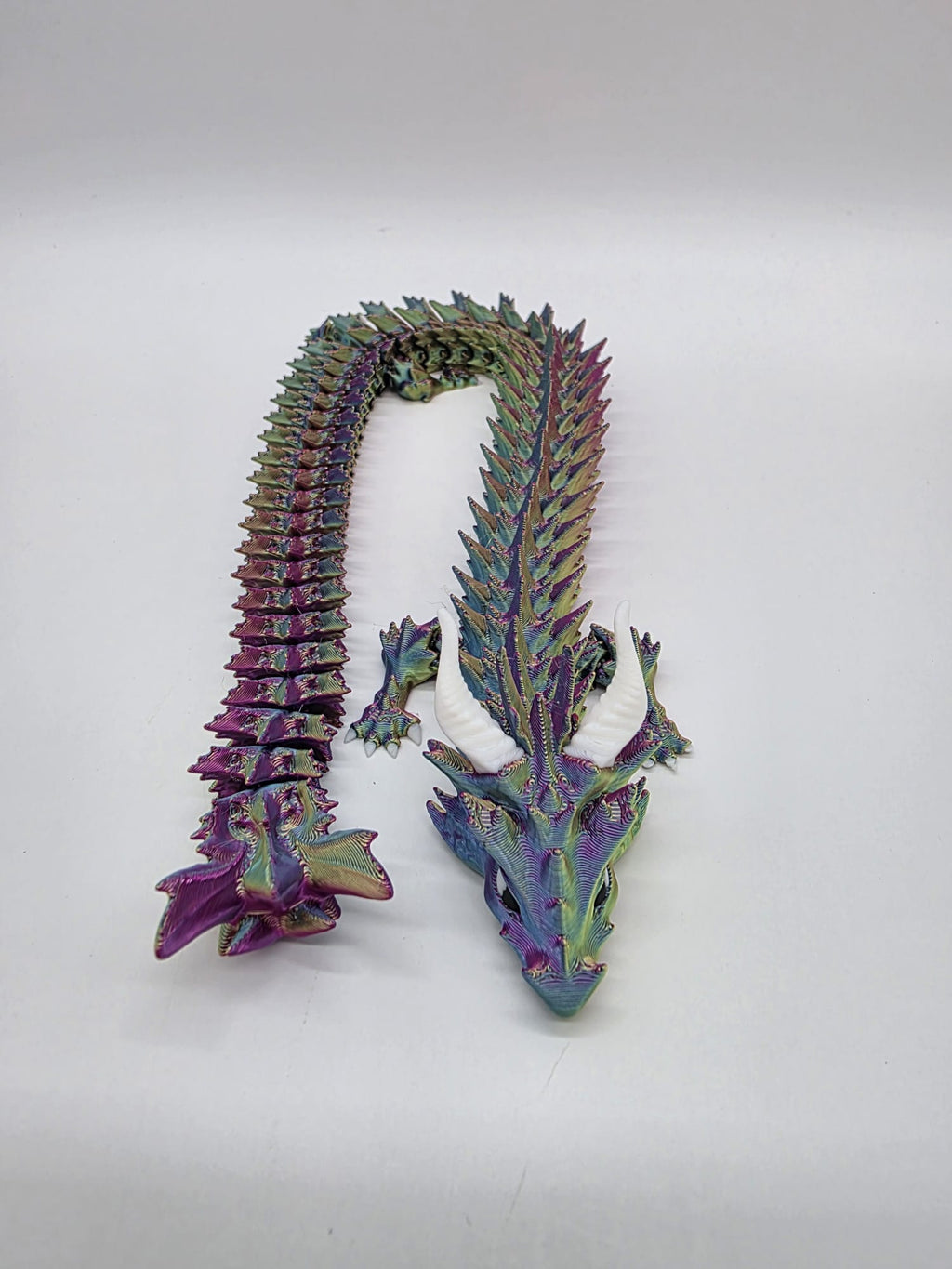 3D-geprinte multicolor flexi draak van circa 30 cm lang met beweegbare staart, schubben en witte hoorns.