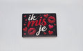 Keramische koelkastmagneet met de tekst Ik mis je, rode hartjes en lippen op een zwarte achtergrond.