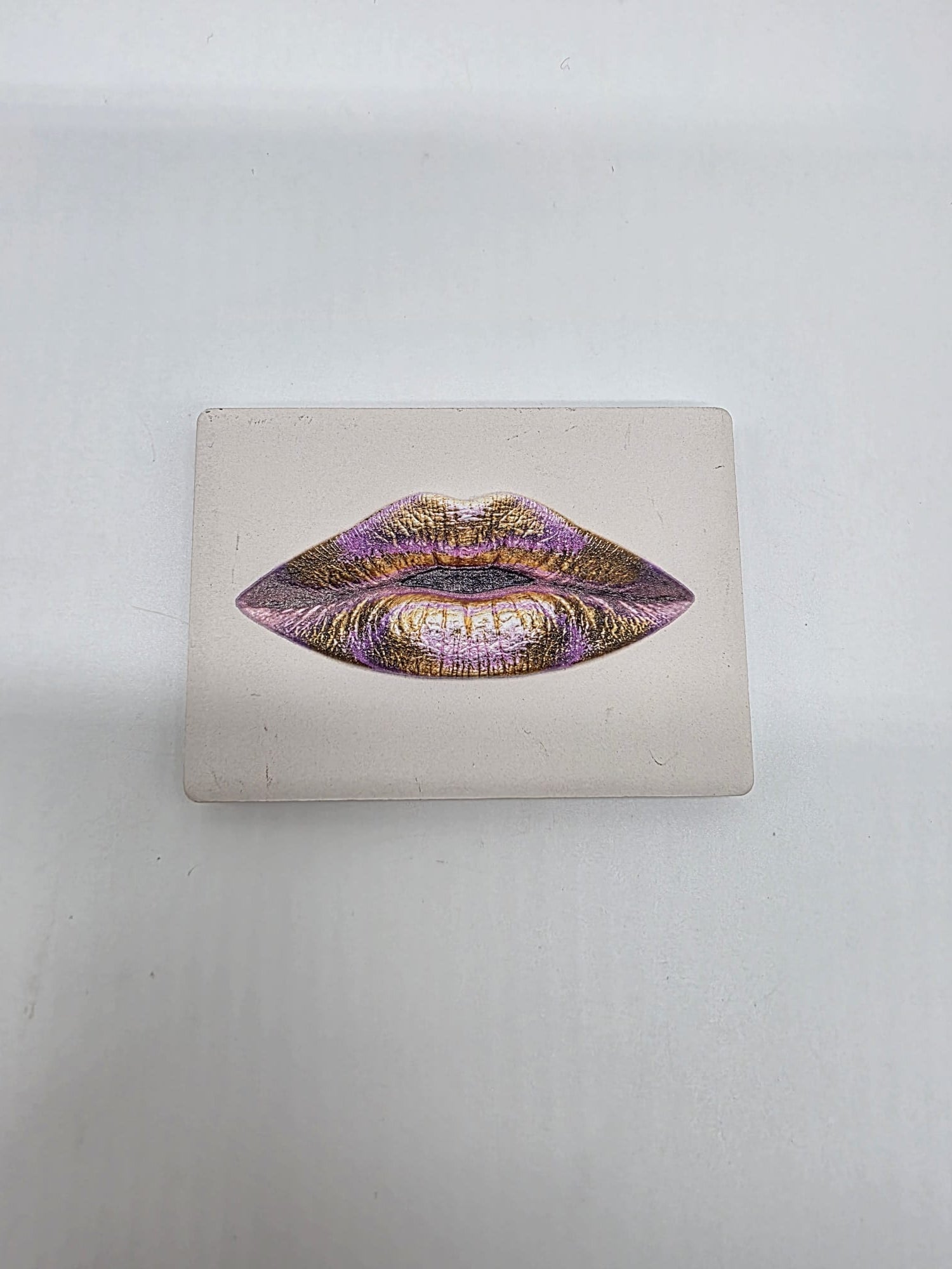 Keramische koelkastmagneet met een artistieke lippenillustratie in roze- en goudtinten op een lichte achtergrond.