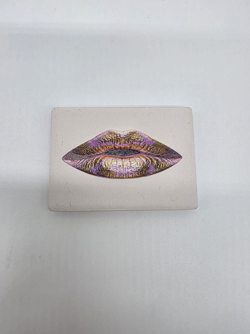 Keramische koelkastmagneet met een artistieke lippenillustratie in roze- en goudtinten op een lichte achtergrond.