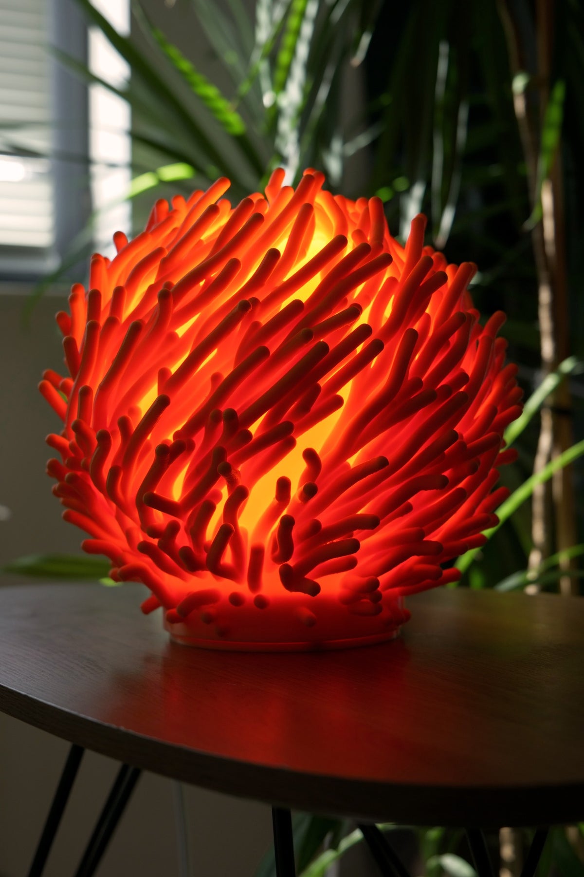 Rode Koraal organische design tafellamp brandend op tafel bij groene planten.