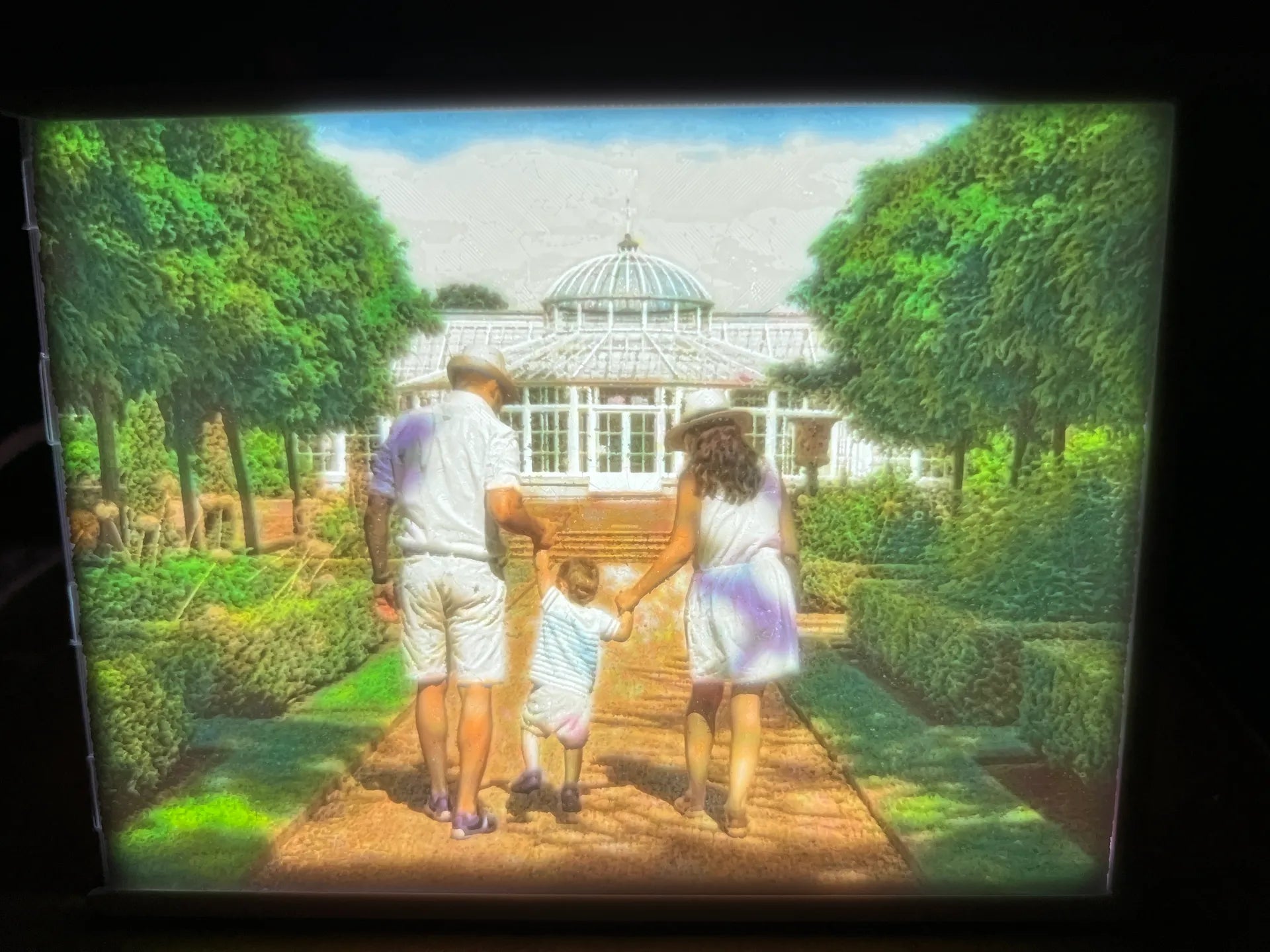 Gepersonaliseerde lithophane fotolamp met verlichte familiefoto van ouders en kind in een groene tuin.