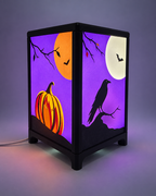 Halloween-tafellamp ingeschakeld, met een oranje pompoen en zwarte raaf op paarse verwisselbare frontjes.
