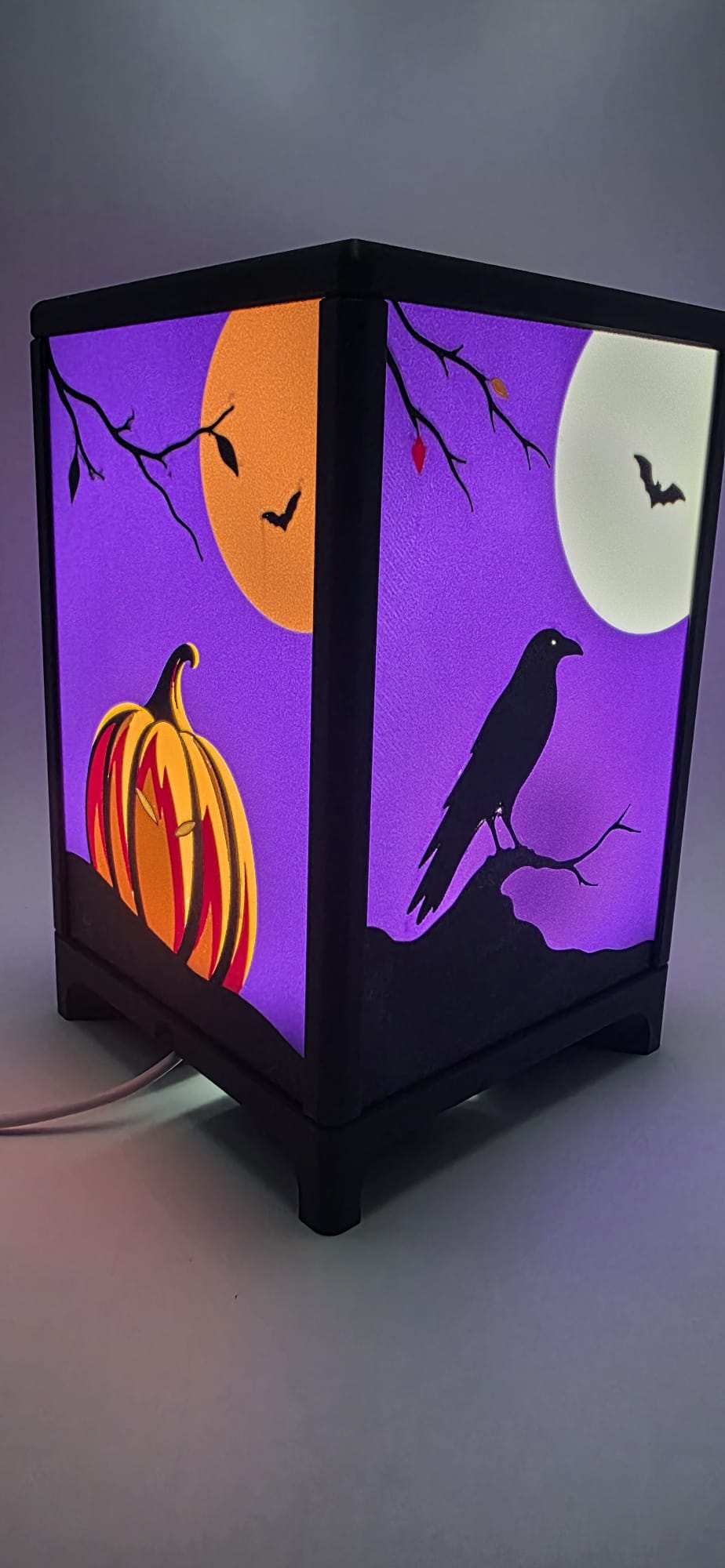 Halloween-tafellamp ingeschakeld, met een oranje pompoen en zwarte raaf op paarse verwisselbare frontjes.