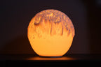 Tide design sfeerlamp brandend tegen een donkere achtergrond met sterk licht- en schaduwspel.