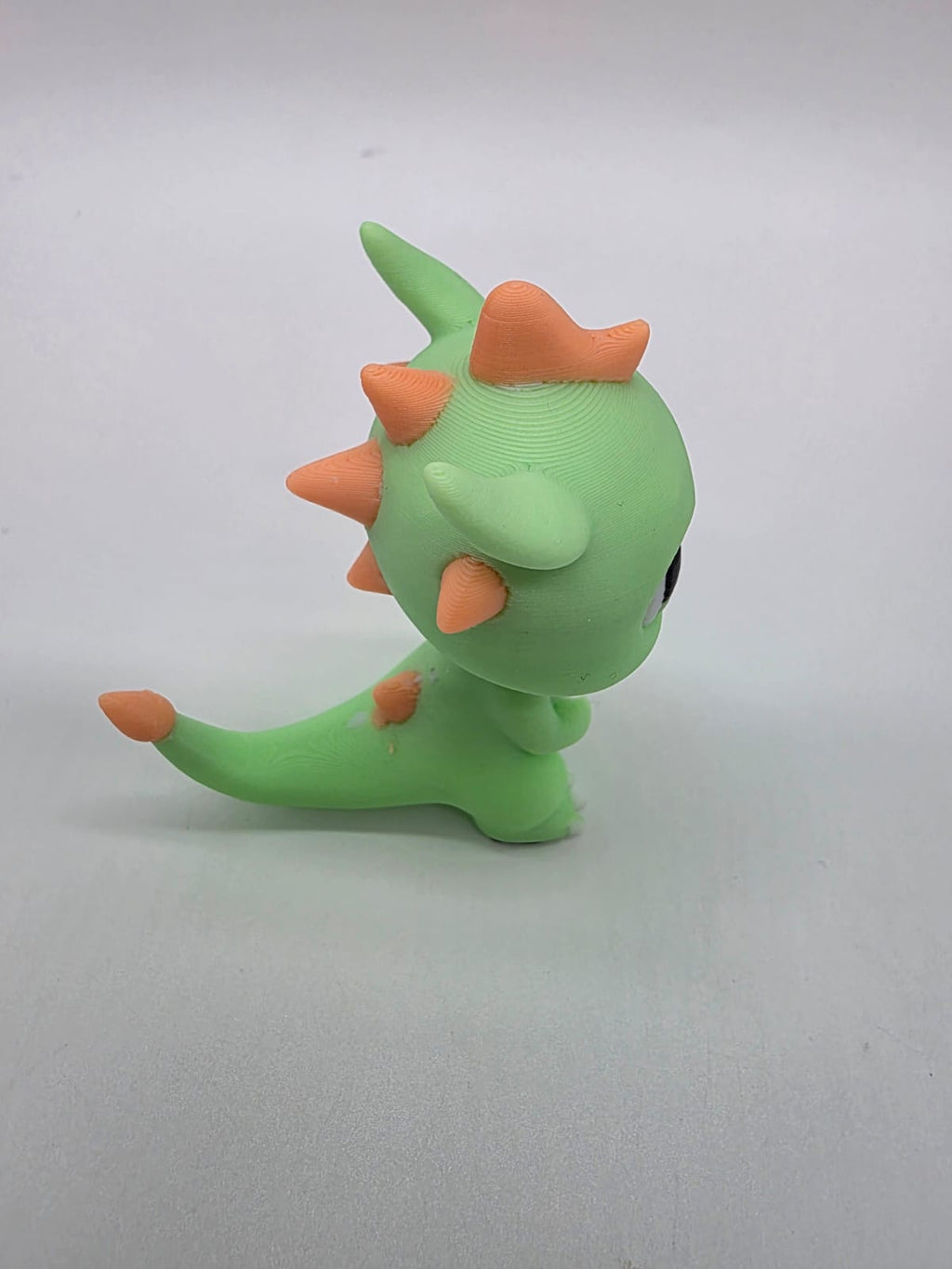 Zijaanzicht van de groene 3D-geprinte draak met oranje stekels en lange staart.