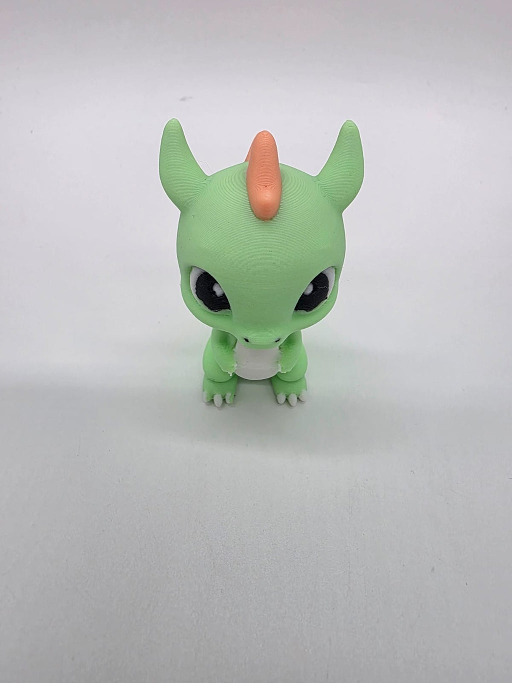 Vriendelijke groene 3D-geprinte draak met oranje, witte en zwarte details.
